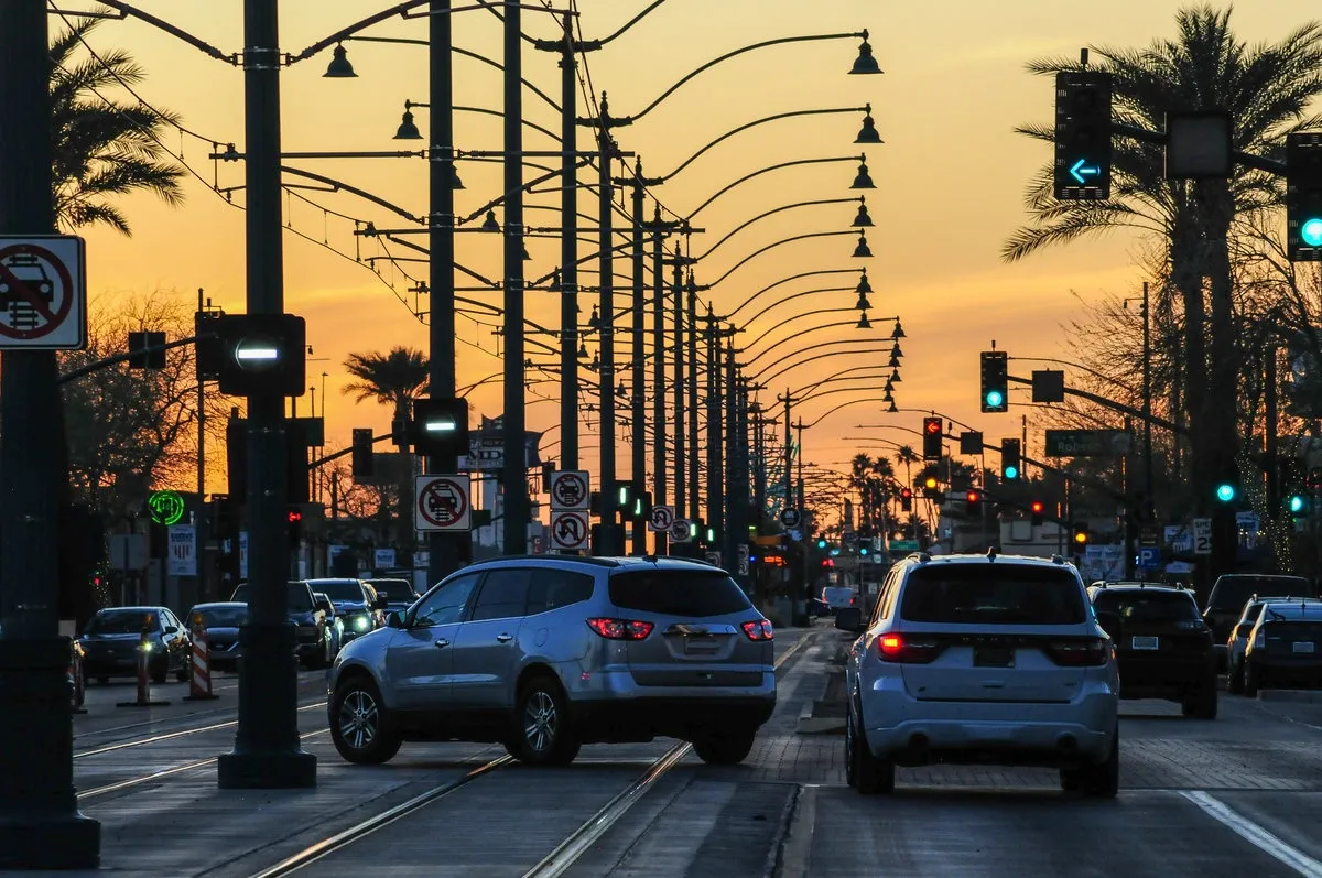 Vehicular traffic on Main Street in downtown Mesa, Arizona, along a long row of streetlights, with golden-yellow sunset light in the background