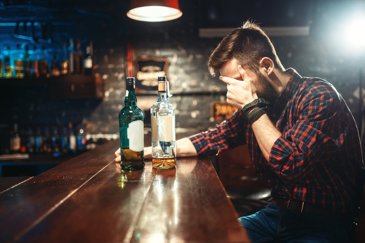 Alcoholic sitting at the bar counter and drinks strong alcohol beverages. Male person in pub, alcoholism, drunkenness