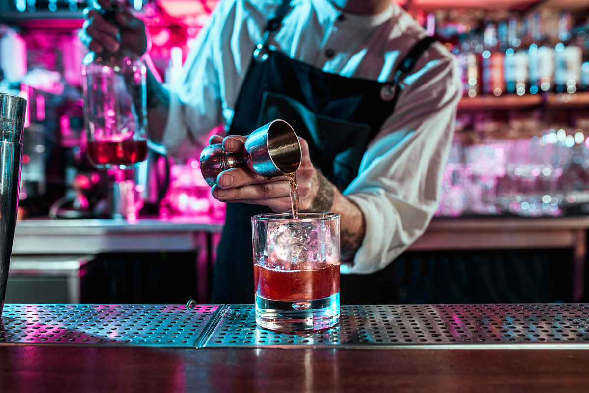 Expert barman is making cocktail at night club or bar. Glass of fiery cocktail on the bar counter against the background of bartenders hands with fire. Barman day concept